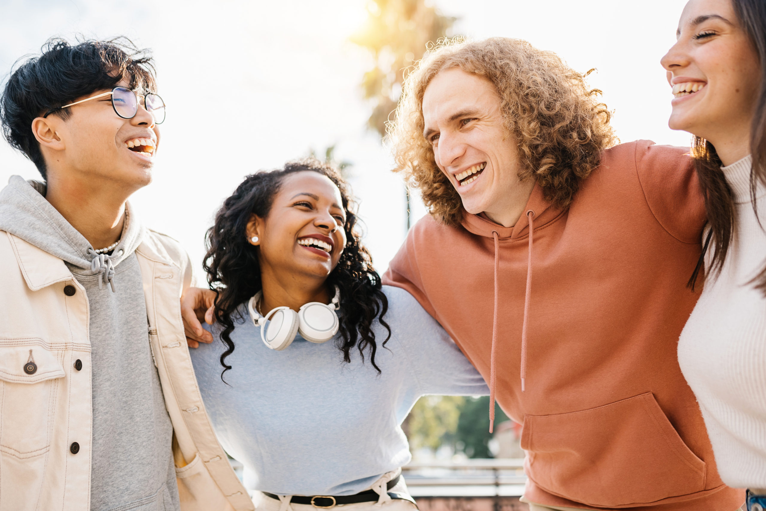 Group of happy young diverse teenage friends laughing together outdoors - Multiracial people having fun while hugging each other in city street during vacation